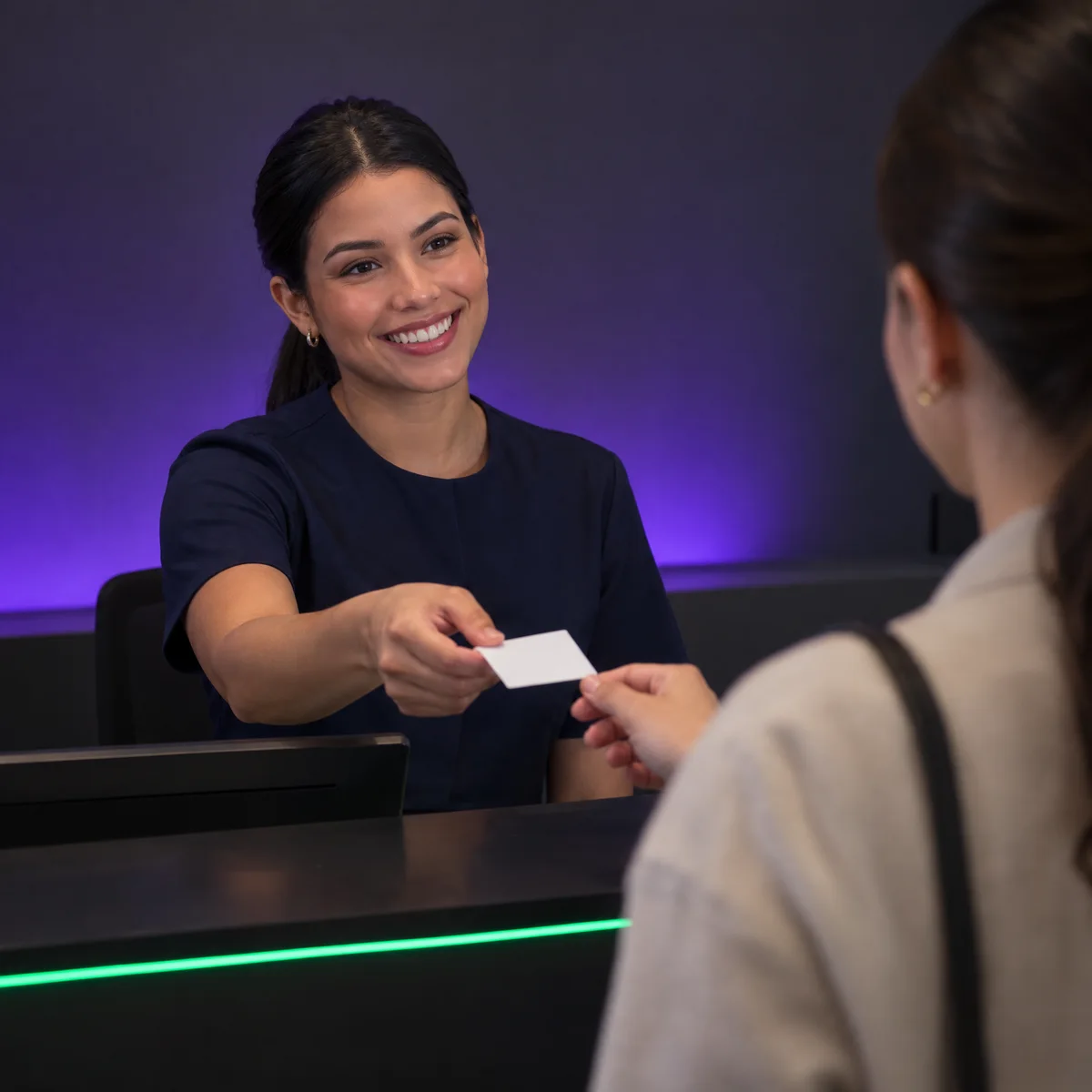 Recepcionista sorrindo entrega um cartão de retorno para a paciente